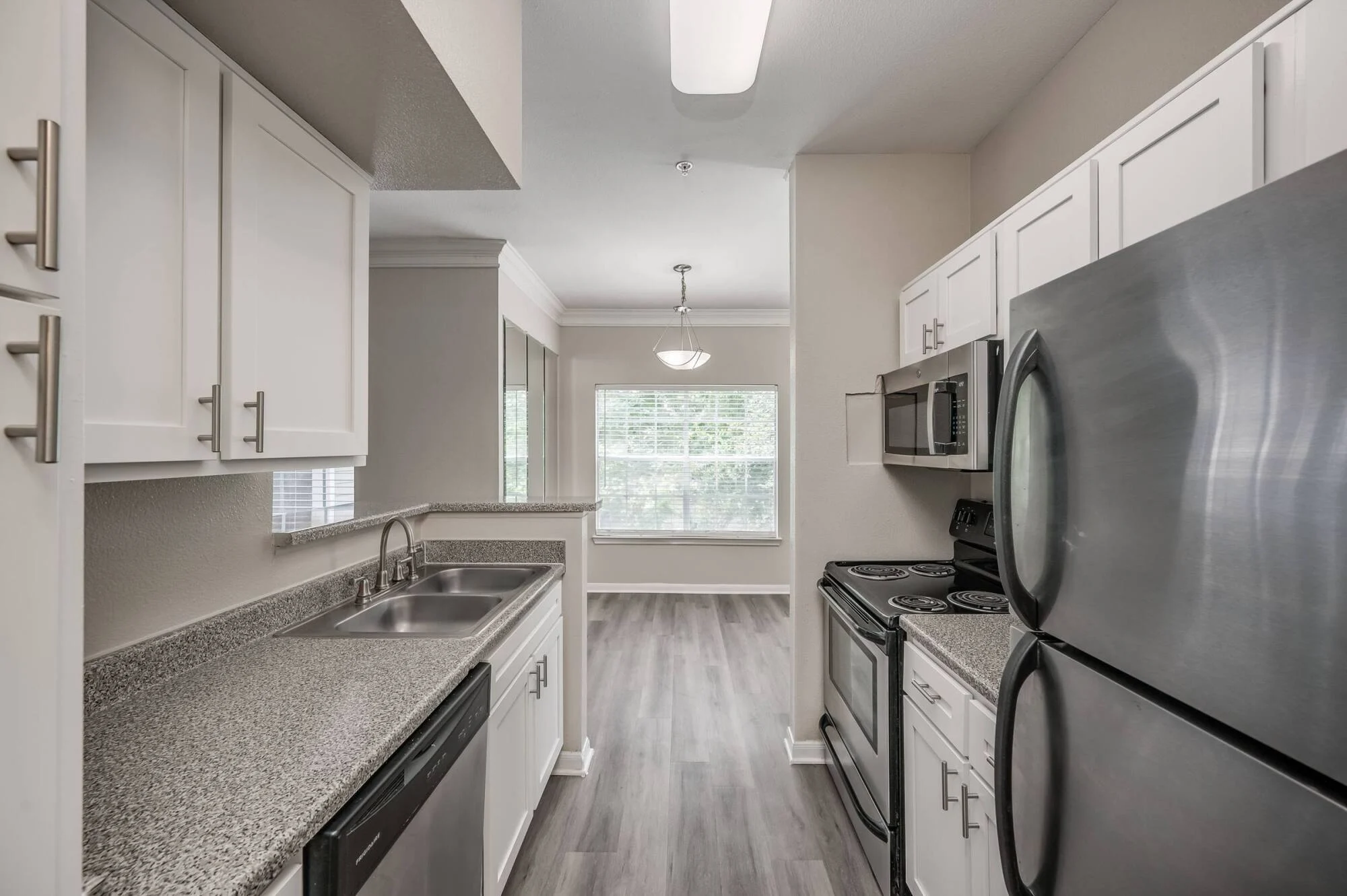 A renovated apartment kitchen at Vinings in Stafford, TX, featuring white cabinets, stainless steel appliances, and a view into the dining area.