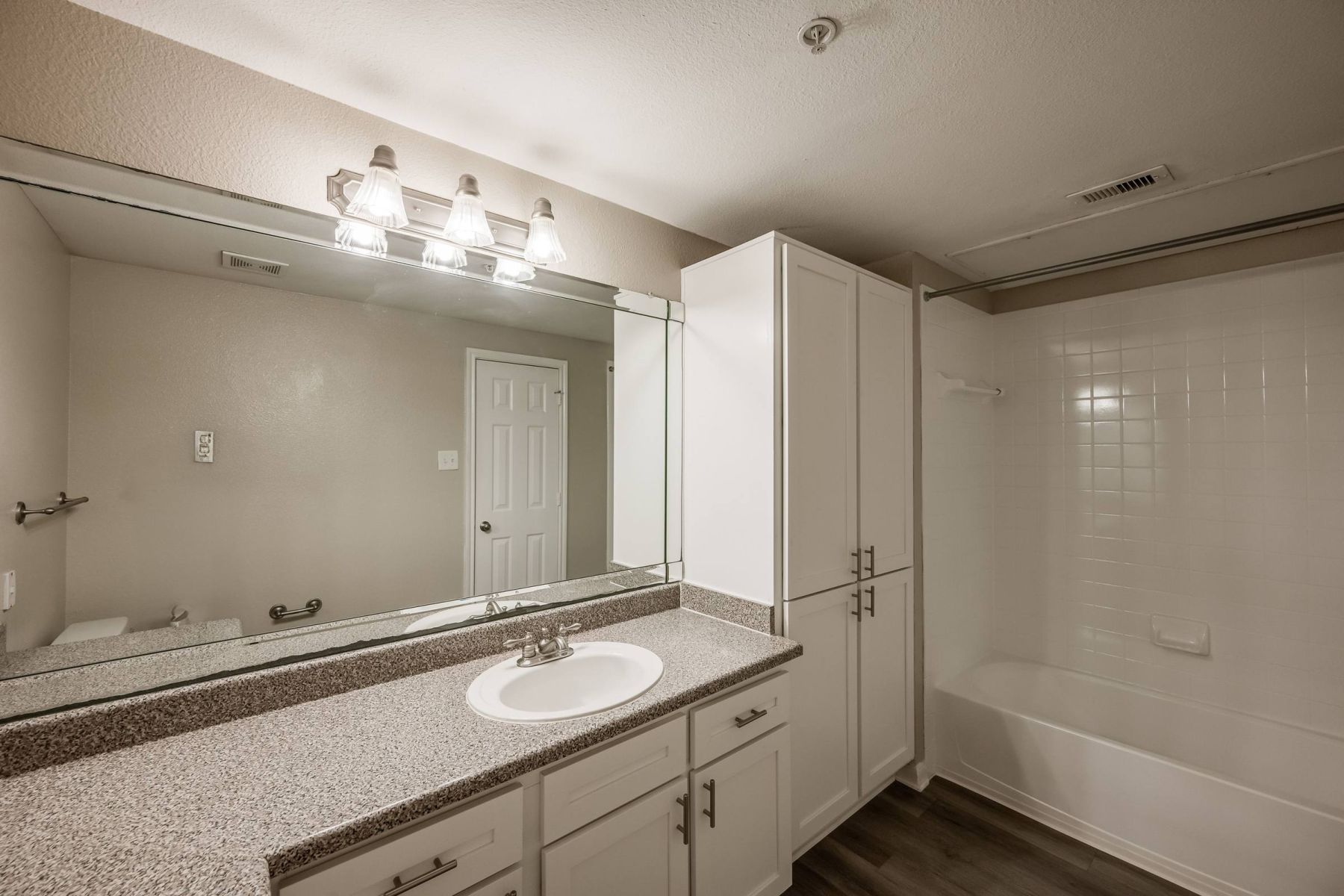 Empty room with wood floors, ceiling fan, and sliding glass door leading to a patio with vertical blinds at Apex West Midown.